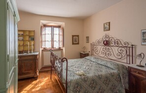 Een slaapkamer met een bed, nachtkastje, dressoir, raam met gordijnen en een boekenkast.