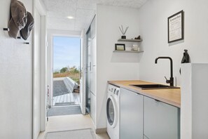 Un lavadero moderno con lavadora, un lavamanos y una puerta que da a un espacio exterior.