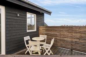 Un bâtiment en bois avec une fenêtre et une terrasse dotée de chaises et d’une table, le tout de couleur blanche.