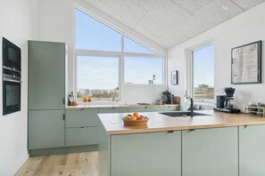 A modern kitchen with a large window, a bowl of fruit on the counter, and a coffee maker. - Stylish energy-efficient holidayhome near by sea (Allingåbro)