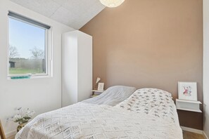 A bedroom with a large window, a bed with a star-patterned bedspread, a bedside table with a lamp, and a framed picture on the wall. - Stylish, energy-efficient holidayhome near by sea (Allingåbro)