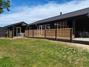 Un bâtiment moderne doté d’un patio couvert, d’un espace extérieur aménagé pour s’asseoir et d’une clôture en bois.