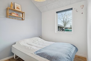 A bedroom with a bed, a window with a view, a shelf with books and a vase, and a wall with a framed picture. - Stylish, energy-efficient holidayhome near by sea (Allingåbro)