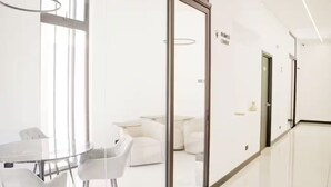 A modern, minimalist hallway with a glass partition, a white sofa, and a table with chairs. - Moon Azul! (guatemala)