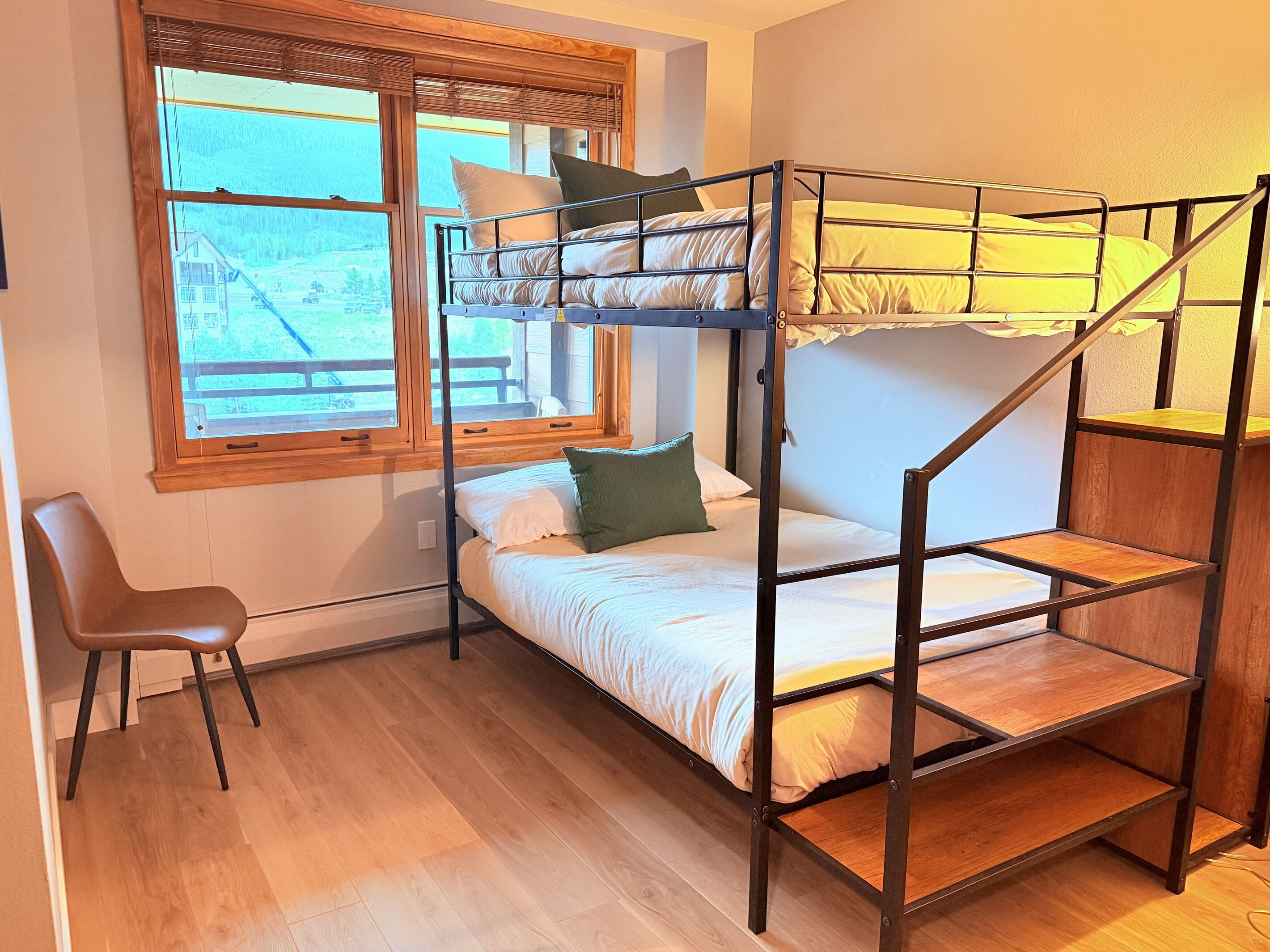 A bunk bed with a wooden frame, a single bed below, and a chair.
