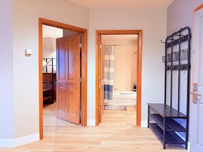 Un pasillo con puertas de madera, un banco de metal negro y un baño visible a través de una puerta abierta.