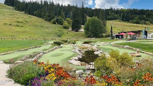 Ein Golfplatz mit Teich, umgeben von bunten Blumen und einer bewaldeten Hügelside.