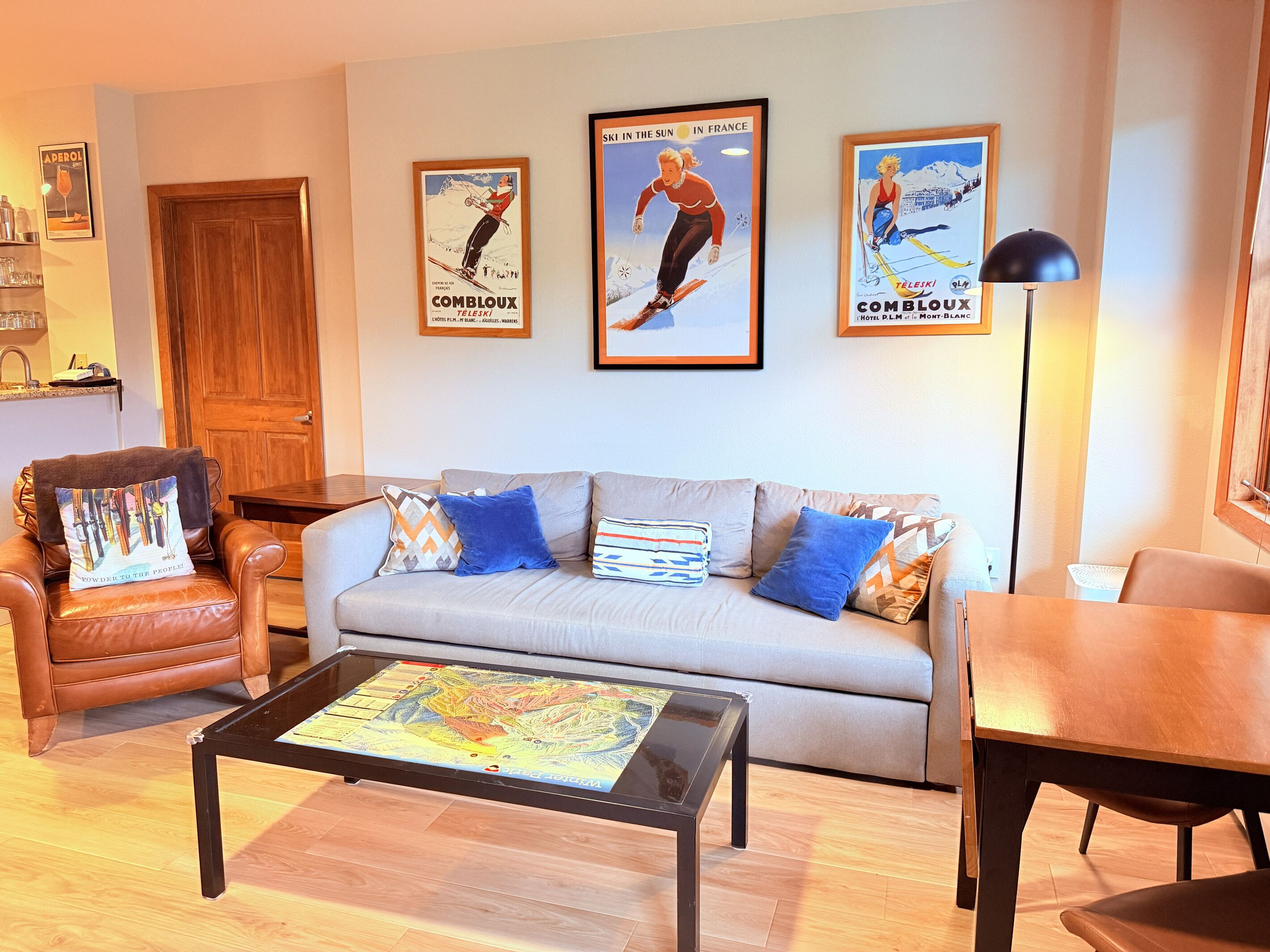 A living room with a sofa, armchairs, a coffee table with a map, and three framed posters on the wall.
