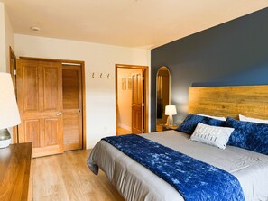 Un dormitorio con cama, puertas de madera, un espejo y una lámpara de noche.