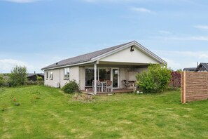 A single-story house with a covered patio, a lawn, and a wooden fence. - Cozy holiday home on Funens north coast (Bogense)