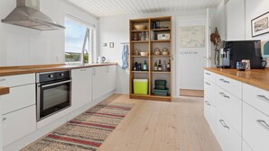 A modern kitchen with white cabinetry, a stainless steel oven, a wooden countertop, and a built-in bookshelf. - Cozy holiday home on Funen’s north coast (Bogense)