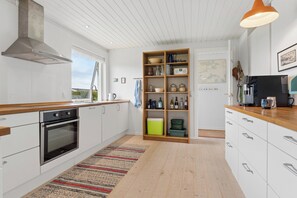 A modern kitchen with white cabinetry, a stainless steel oven, a wooden countertop, and a built-in bookshelf. - Cozy holiday home on Funen’s north coast (Bogense)