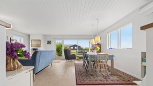 A spacious room with a dining area, a sofa, and a view of the outside. - Cozy holiday home on Funen’s north coast (Bogense)