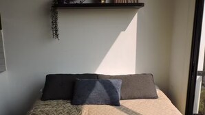 Una camera da letto con un letto, cuscini, una sveglia, un vaso e un cartello su uno scaffale.