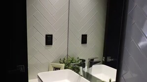 Un bagno moderno con zoccolo a mosaico bianco a spina di pesce, un lavandino bianco e uno specchio grande.