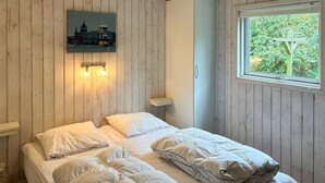 A bedroom with a bed, pillows, a nightstand, a wall-mounted light, and a window with a view of greenery. - Lovely home in Væggerløse with sauna (Væggerløse)