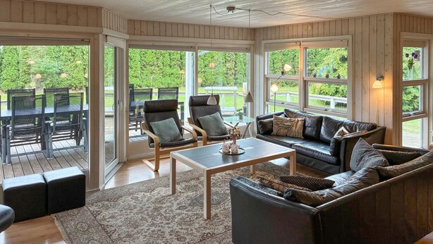 A spacious living area with a large window, a sofa, a coffee table, and a dining set. - Lovely home in Væggerløse with sauna (Væggerløse)