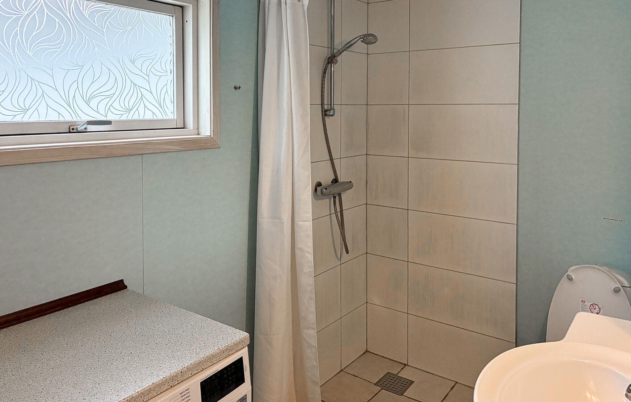 A bathroom with a shower, a toilet, and a window with frosted glass.