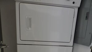 Eine weiße Waschmaschine mit Bedienfeld oben, platziert in einem Raum mit Tür und einem kleinen Schrank.