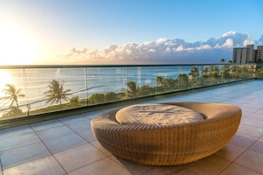 A balcony with a wicker chair, a glass railing, and a view of the ocean and palm trees. - Honua Kai | Ocean Front 3 BR | Free Car w/ 6+ Nights | HKH-501 (Lahaina)