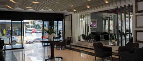 A modern lobby with a wavy ceiling design, a reception desk, seating area, and large glass doors leading outside.