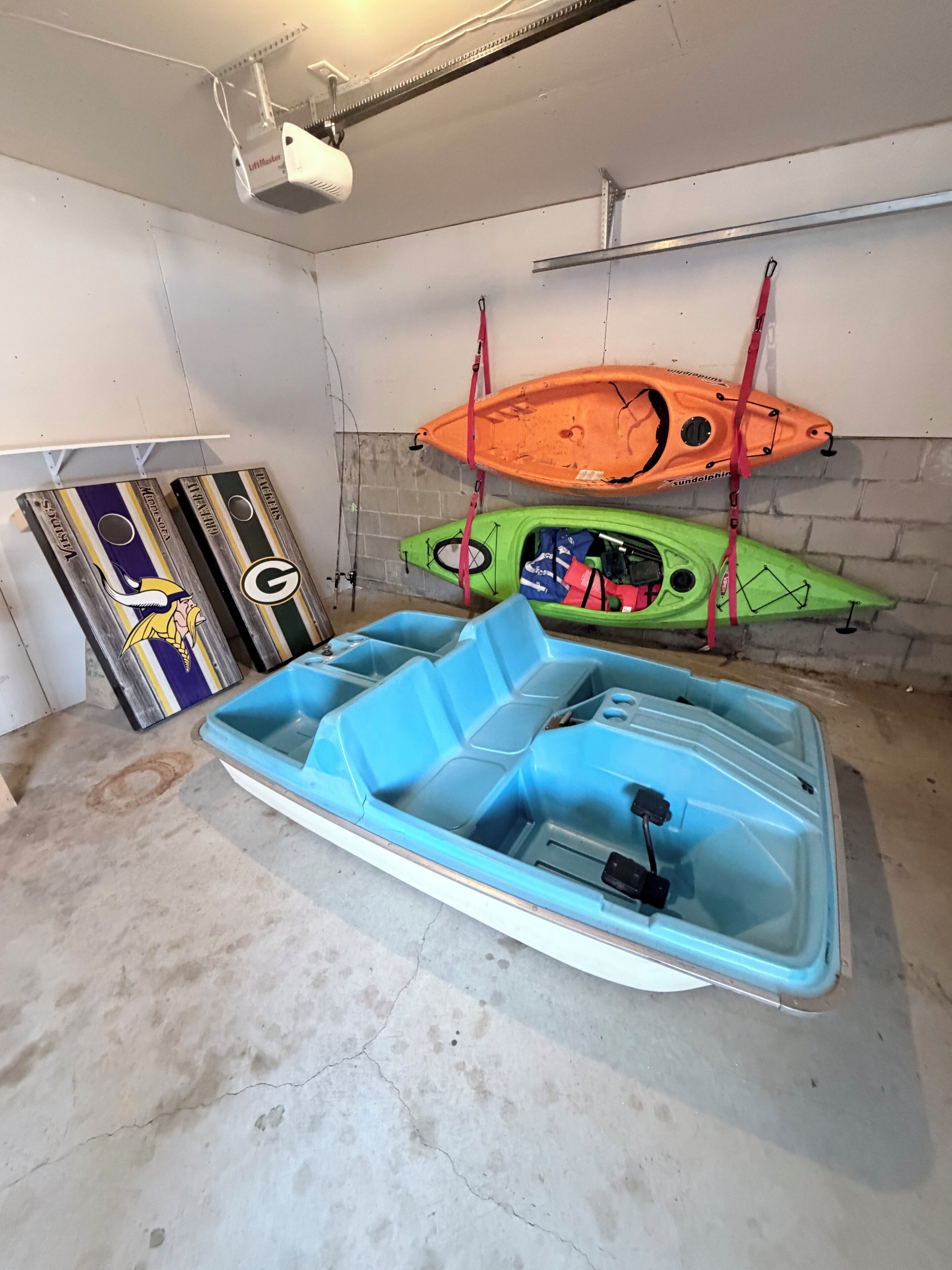Un garage con kayak e una barca su supporti, pavimento in cemento e un proiettore a soffitto.
