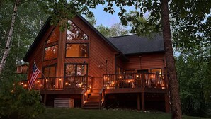 A large wooden cabin with a balcony, a flag, and a clock. - NEW Sunset Serenity Lakefront Cabin wSauna & Private Dock: Kego Lake - Sleeps 10 (Fifty Lakes)