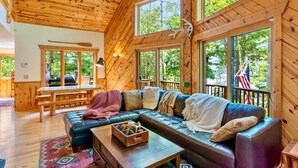 Een gezellig cabin interieur met houten plafond, grote ramen, een leren bank en een eethoek.