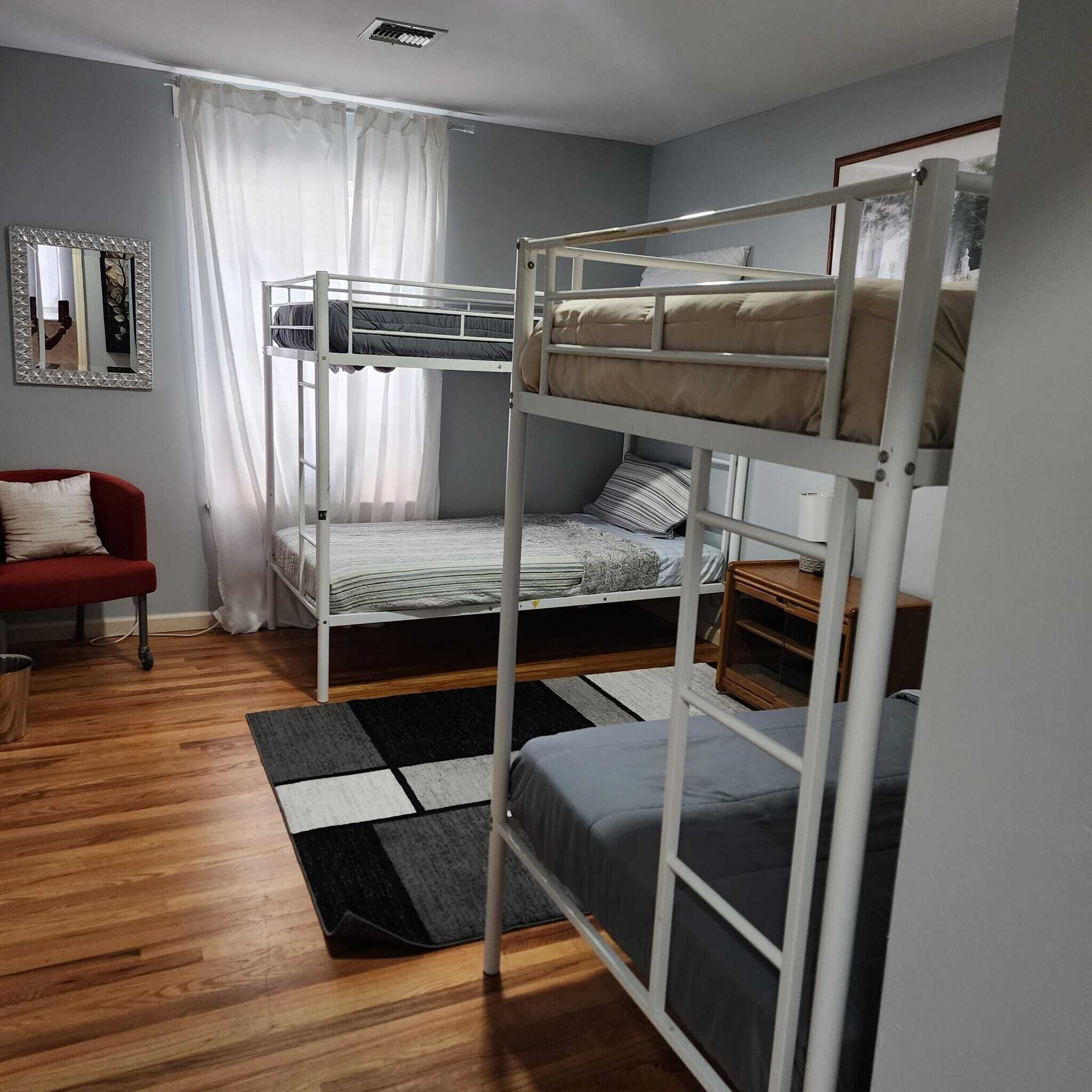 Une chambre avec un lit superposé, une chaise rouge, un miroir et une fenêtre avec des rideaux.