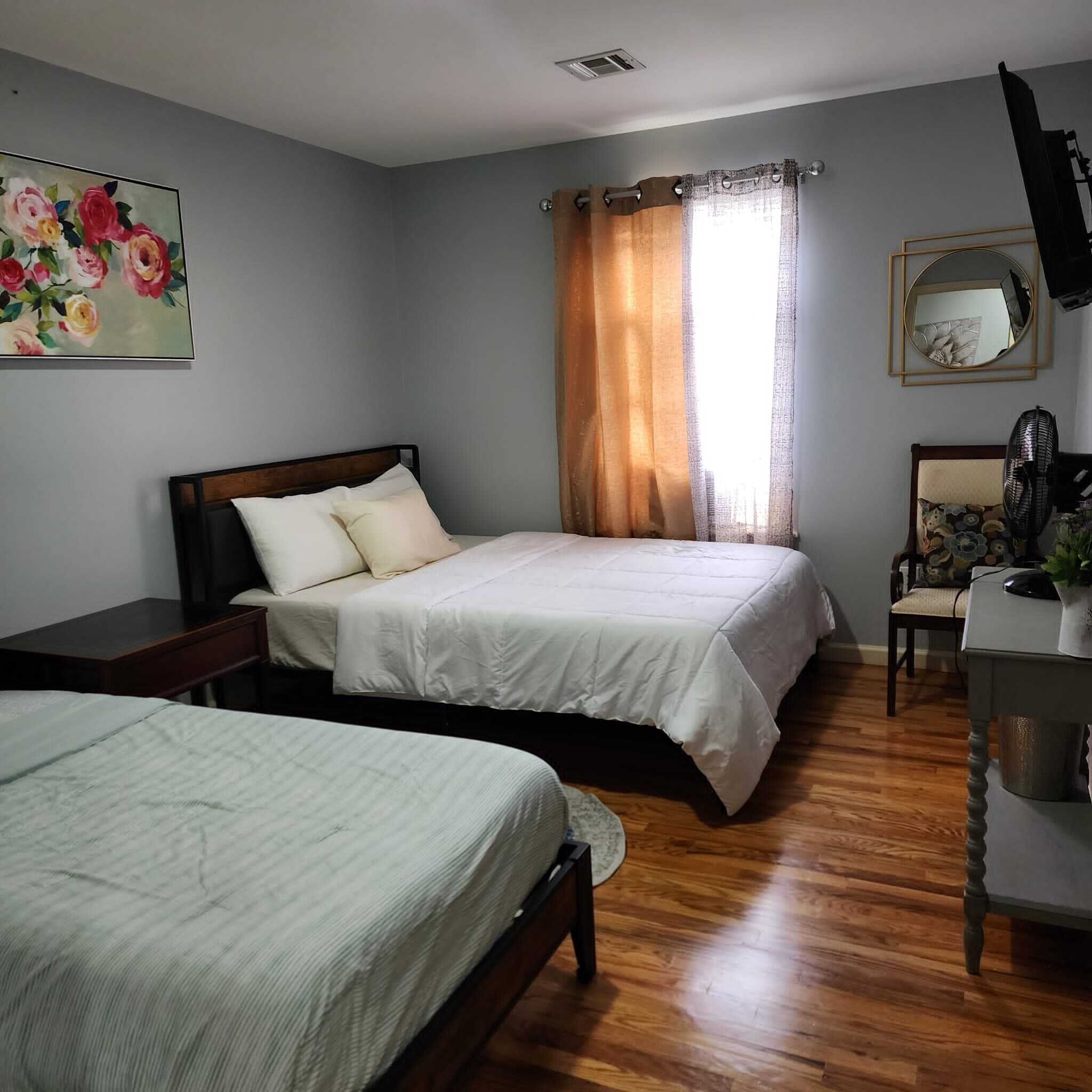 A bedroom with two beds, a desk, a chair, a mirror, and a painting on the wall.