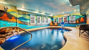 En inomhuspool med en väggmålning, ett bubbelbad och två solstolar.