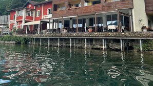 Un edificio frente al agua con una terraza de restaurante, escalones de piedra que bajan hacia el mar y el reflejo del edificio en el agua.