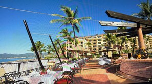 An outdoor dining area with tables and chairs, umbrellas, and palm trees. - Beautiful hotel suite with AC, beach access & fitness room in amazing Nayarit MX (Nay.)