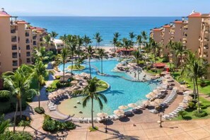 A resort with a central pool surrounded by palm trees and lounge chairs, overlooking the ocean. - Beautiful hotel suite with AC, beach access & fitness room in amazing Nayarit MX (Nay.)