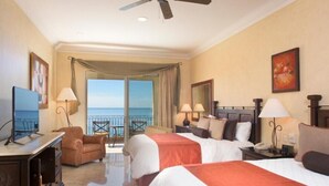 A hotel room with two beds, a desk with a TV, a chair, a balcony with a view of the sea, and a ceiling fan. - Beautiful hotel suite with AC, beach access & fitness room in amazing Nayarit MX (Nay.)