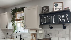 A kitchen with white cabinets, a coffee bar sign, a sink, and a countertop with snacks. - One story 4 bedroom updated ranch in the middle of it all. (Simpsonville)
