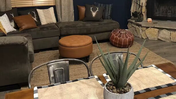 Ein gemütliches Wohnzimmer mit einer dunkelblauen Wand, einem Kamin aus Stein, einer Couch mit gemusterten Kissen und einem Couchtisch mit einem Blumentopf.