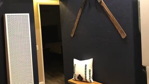 Ein Flur mit dunkler Wand, einer Holzbank, einem Kissen mit Baummuster und zwei an der Wand gelehnten Ski.