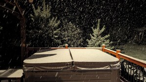 A covered outdoor seating area with a wooden railing, surrounded by snow-covered trees. - large ski ranch hot tub close to killington pets ok (Mendon)