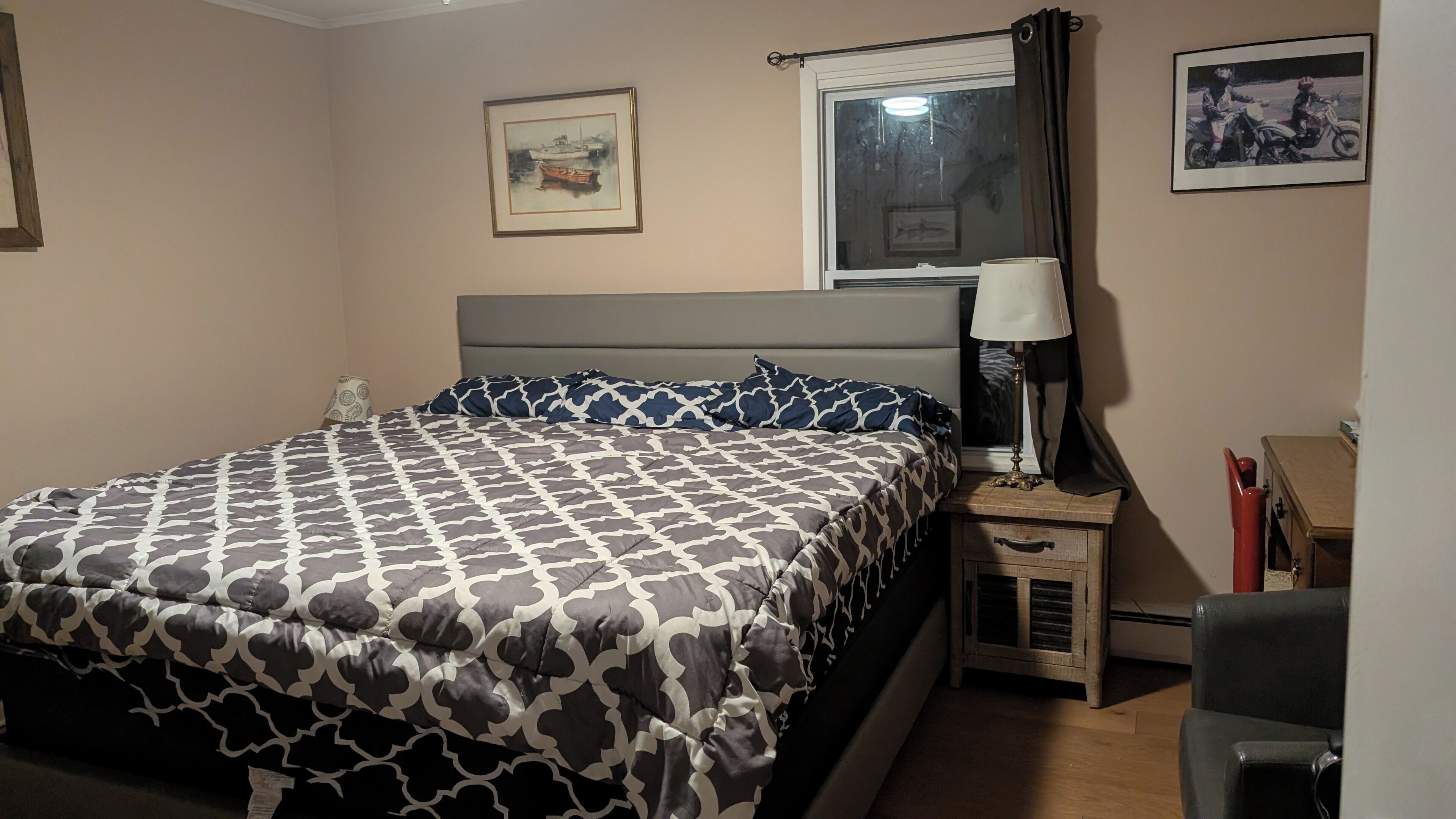 A neatly made bed with patterned bedding, a bedside table with a lamp, and a window with curtains.