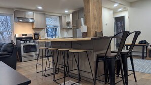 A modern kitchen with a central island, bar stools, a stove, and a refrigerator. - large ski ranch hot tub close to killington pets ok (Mendon)