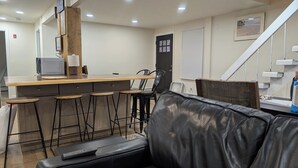 A modern kitchen with a wooden counter, bar stools, and a black leather couch. - large ski ranch hot tub close to killington pets ok (Mendon)