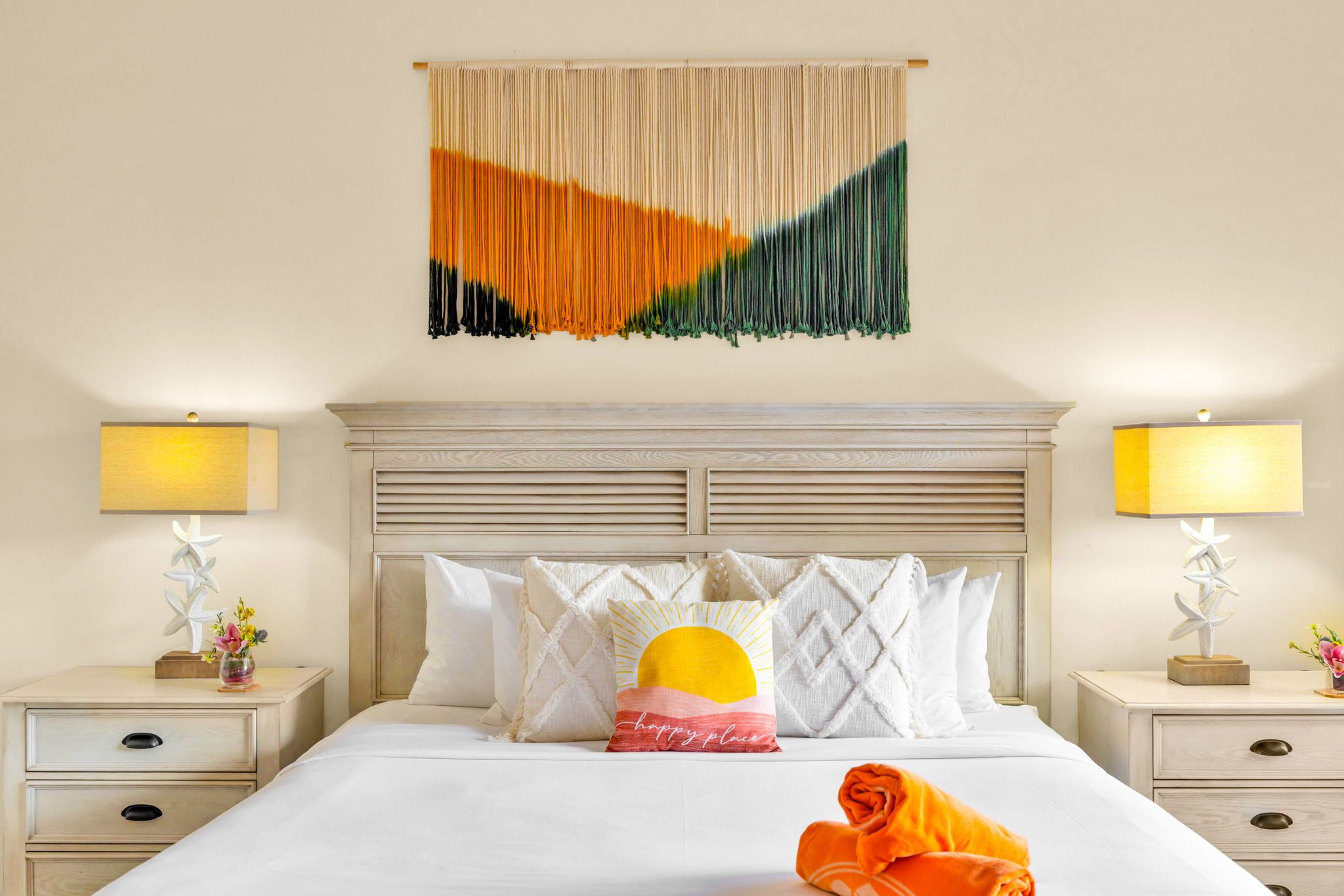 A hotel room with a bed, two bedside tables, a headboard, a wall hanging, and a lamp.