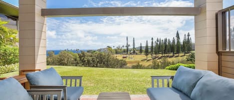 A covered patio with outdoor furniture, a view of a golf course, and a clear sky.