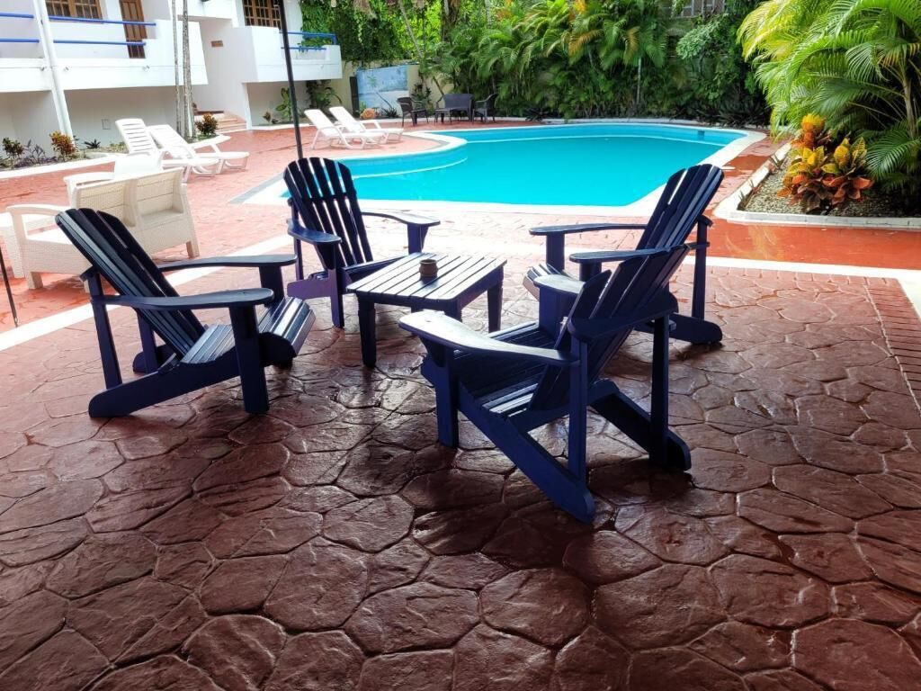 A pool area with blue Adirondack chairs and a tiled patio.