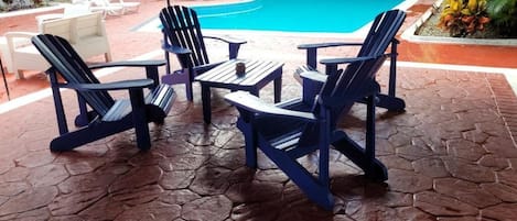 A pool area with blue Adirondack chairs and a tiled patio.