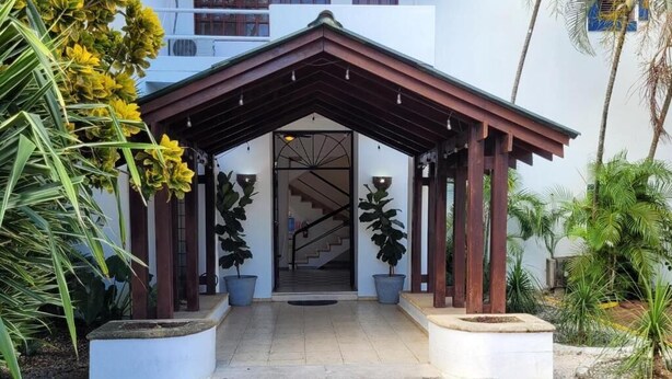 Une entrée abritée, avec un escalier menant à un bâtiment, le tout entouré de plantes en pot.