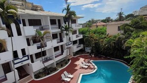 Un espace piscine avec des chaises longues et un bâtiment doté de nombreux balcons.