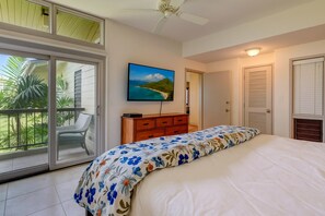Ein Schlafzimmer mit Bett, Kommode, Fernseher und einem Balkon mit Blick auf Grünflächen.