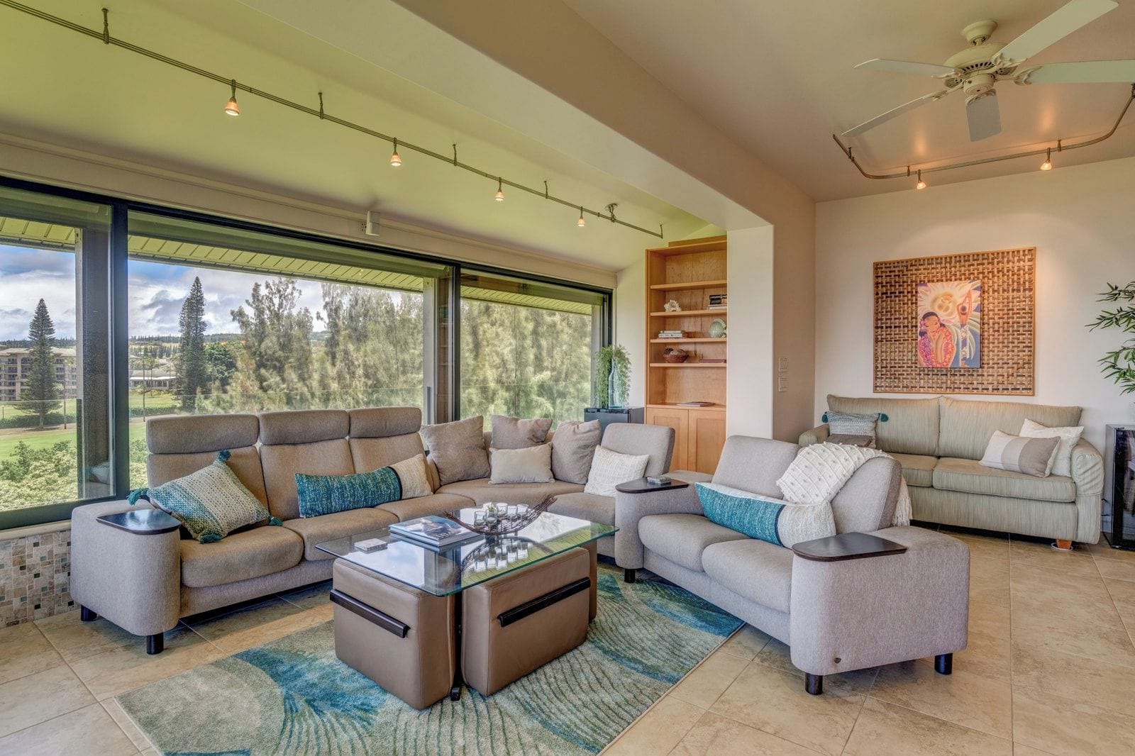 A spacious living room with a large window, a sofa set, a coffee table, and a bookshelf.